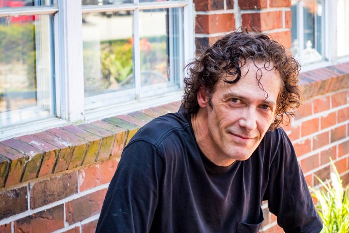 Dr. Kevin J. Payne, seated outdoors by a brick wall and window