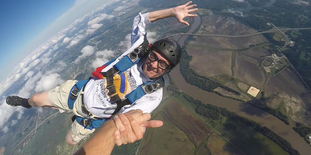Dr. Payne holding a grip with another skydiver in freefall above a river valley