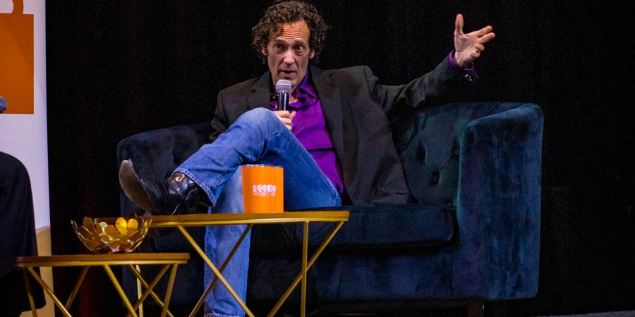 Dr. Kevin J. Payne on stage in an armchair, microphone in hand, gesturing as he speaks